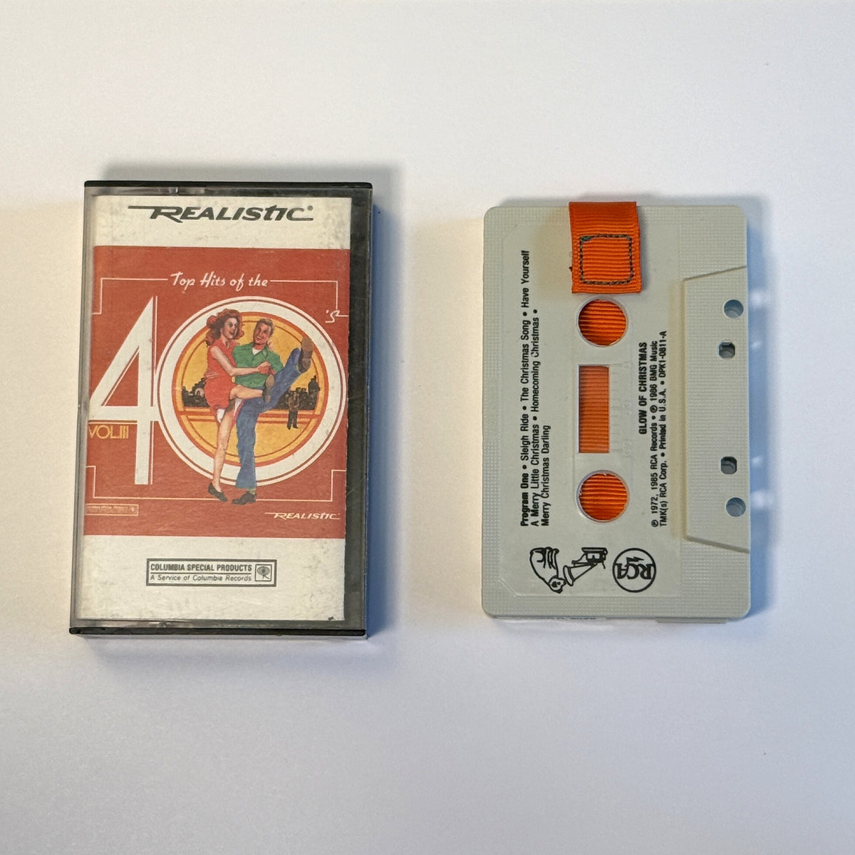 Glow of Christmas gray cassette wallet with an orange pull tab beside a Realistic Top Hits of the 40s case