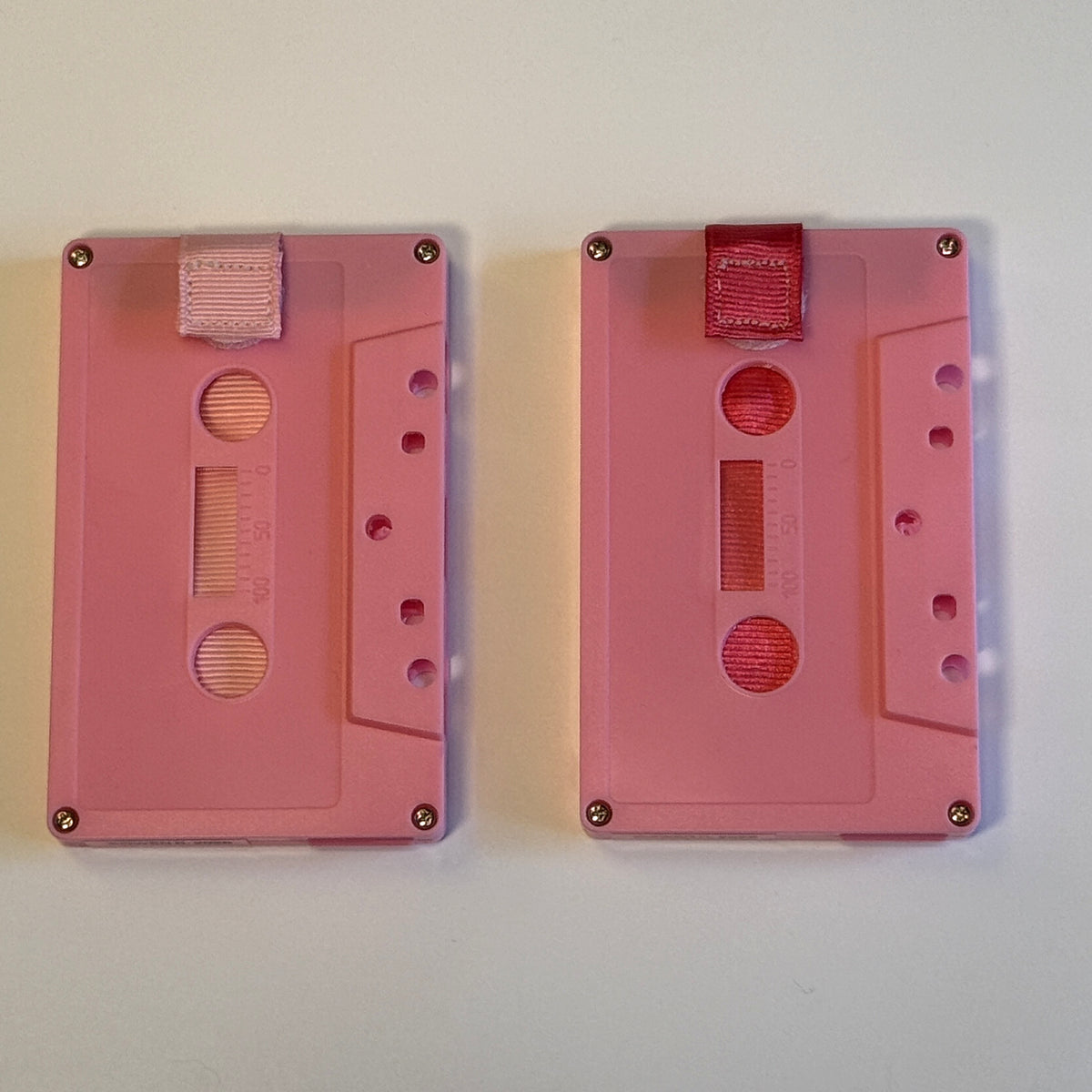Two solid pink cassette wallets side by side with light pink and deep pink pull straps