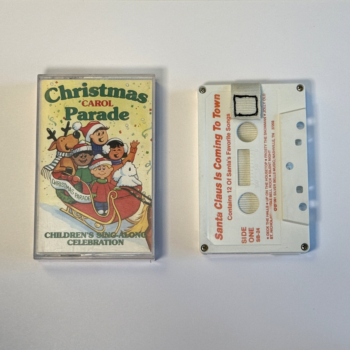 Santa Claus Is Coming to Town white cassette wallet with white pull tab beside a Christmas Carol Parade case